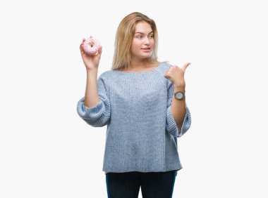 İşaret ve başparmak kadar mutlu yüz gülümseyen tarafı ile gösteren izole arka plan üzerinde tatlı çörek yiyen genç kafkas kadın