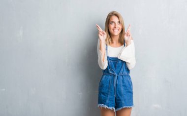 Umut ve gözleri kapalı geçiş parmaklarıyla gülümseyen grunge gri duvar üzerinde duran güzel genç kadın. Şans ve batıl kavramı.