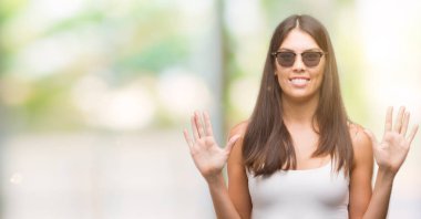 Number ten kendinden emin ve mutlu gülümseyerek sırasında gösterilen ve parmakları ile işaret genç güzel İspanyol giyen güneş gözlüğü.