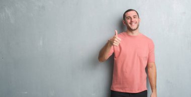 Beyaz delikanlı hareketi el ile mutlu yaşasın yapıyor gri grunge duvarın üzerinden. Kameraya bakarak başarı gösteren ile ifade onaylama.