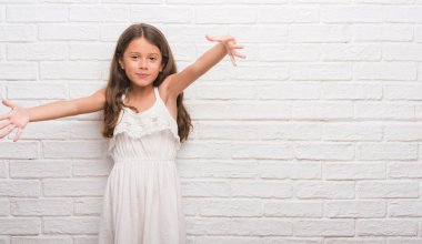 Sarılmak için kollarını açarak gülümseyerek kameraya bakarak beyaz tuğla duvarın üzerinden genç İspanyol çocuk. Neşeli ifade kucaklayan mutluluk.