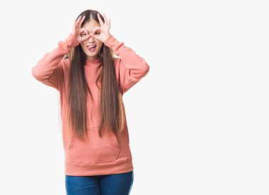 Spor sweathshirt dilini, parmaklarının arasından baktığını yapışmasını dürbün gibi ok jest yapıyor giyen izole arka plan üzerinde Genç Çinli kadın. Deli ifade.