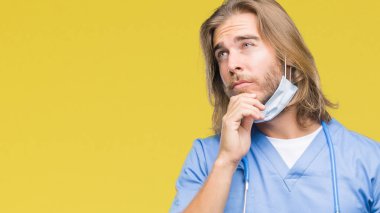 Genç yakışıklı adam uzun saçlı çene düşünme hakkında soru, dalgın ifade üzerine el ile izole arka plan üzerinde doktor. Düşünceli yüzüyle gülümsüyor. Şüphe kavramı.