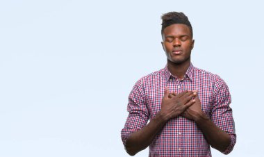 Göğüs kapalı gözler ve yüzünde minnettar jest ile genç Afro-Amerikan adam ile gülümseyen izole arka plan üzerinde eller. Sağlık kavramı.