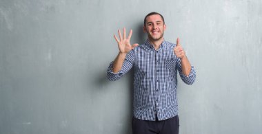 Beyaz delikanlı gösterilen ve parmakları ile işaret gri grunge duvarın üzerinden 6 kendinden emin ve mutlu gülümseyerek iken numara.