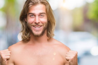 Genç yakışıklı gömleksiz adam uzun saçlı seksi vücut izole arka plan kutlama üzerinde gösterilen şaşırttı ve başarı için kaldırdı kollarını açarak hayret ve gözleri açık. Kazanan kavramı.