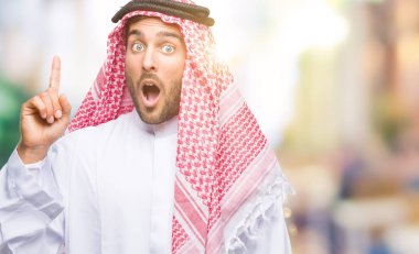 Başarılı fikirle izole arka plan işaret parmağı üzerinde keffiyeh giyen genç yakışıklı adam. Çıktıktan ve mutlu. Bir numara.