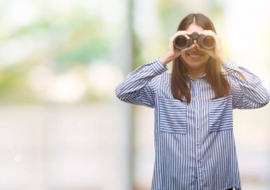 Dürbün ile ayakta ve diş gösterilen kendine güvenen bir gülümsemeyle gülümseyerek mutlu bir yüz tutan genç İspanyol kadın