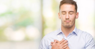 Yakışıklı genç işadamı elleri göğsünde gözleri kapalı gülümsüyor ve yüzünde minnet ifadesi var. Sağlık kavramı.