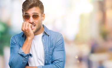 Genç yakışıklı adam stresli ve gergin ile izole arka plan üzerinde güneş gözlüğü takıyor tırnak ısırma dudaklarından eller. Anksiyete sorunu.