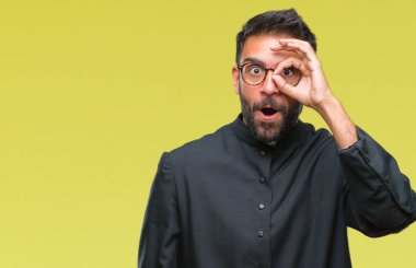 Sürpriz yüz, göz parmaklarının arasından seyir yetişkin İspanyol Katolik rahip adam ok jest yapıyor izole arka plan üzerinde şok. İmansız ifade.