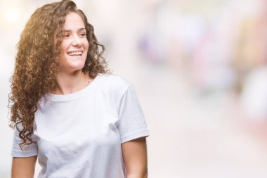 Güzel esmer kıvırcık saçlı Genç kız rahat t-shirt giyen izole arka plan uzak tarafına gülümseme ile yüzünde, doğal ifade inceliyorlar. Kendine güvenen gülüyor.