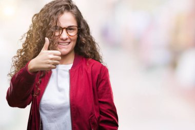 Güzel esmer kıvırcık saçlı Genç kız mutlu yaşasın el ile jest yapıyor izole arka plan üzerinde ceket ve gözlük takıyor. Kameraya bakarak başarı gösteren ile ifade onaylama.