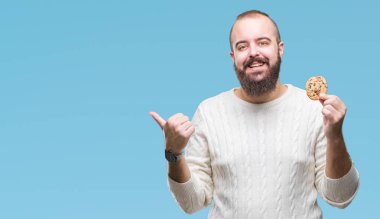 Genç hipster man işaret ve başparmak kadar mutlu yüz gülümseyen tarafı ile gösteren izole arka plan üzerinde çikolata çerez yemek