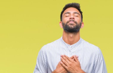 Göğüs kapalı gözler ve yüzünde minnettar jest ile yetişkin İspanyol adam ile gülümseyen izole arka plan üzerinde eller. Sağlık kavramı.