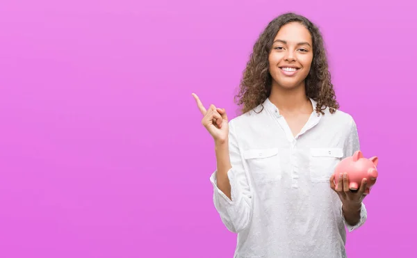 Junge Hispanische Frau Hält Sparschwein Sehr Glücklich Und Zeigt Mit — Stockfoto