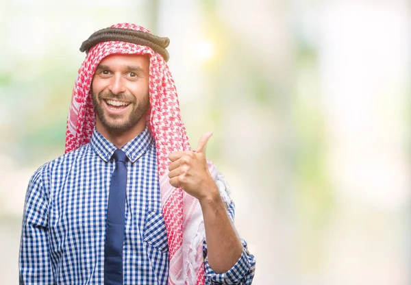 Young handsome arabian business man wearing keffiyeh over isolated background doing happy thumbs up gesture with hand. Approving expression looking at the camera with showing success.