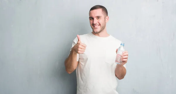 Kaukasische Jongeman Grijs Grunge Muur Holding Fles Water Blij Met — Stockfoto