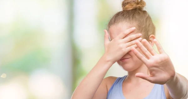 Young blonde woman covering eyes with hands and doing stop gesture with sad and fear expression. Embarrassed and negative concept.