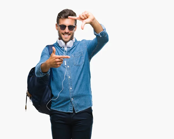 笑顔の幸せそうな顔で指と手作りフレーム分離の背景にヘッドフォンとバックパックを着た若いハンサムな観光客男 創造性と写真のコンセプト — ストック写真