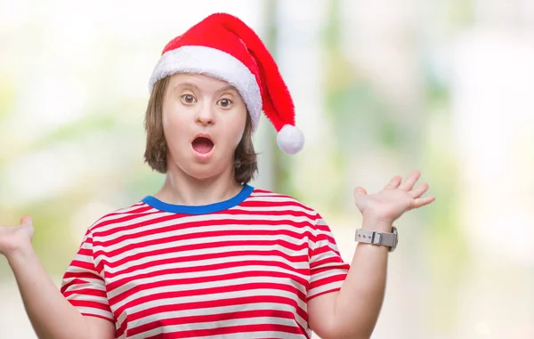 上クリスマス帽子をかぶっているダウン症候群の若い大人の女性は 腕と手を上げて背景無知と混乱して式を隔離しました 疑いのコンセプト — ストック写真