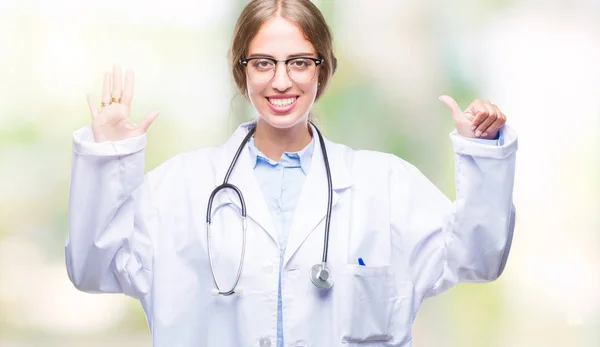 美丽的年轻金发碧眼的医生妇女穿着医疗制服在孤立的背景显示和手指第六 而微笑着自信和快乐 — 图库照片