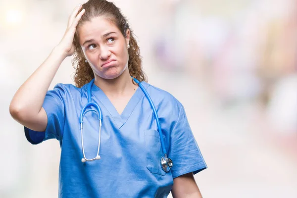 Young brunette doctor girl wearing nurse or surgeon uniform over isolated background confuse and wonder about question. Uncertain with doubt, thinking with hand on head. Pensive concept.
