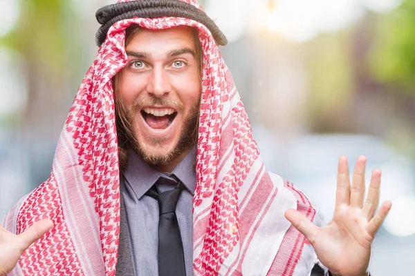 クーフィーヤを着て長い髪をした若いハンサムなアラビア人クレイジーを祝う背景を分離した腕を上げると成功のためびっくりし 叫んで興奮して目を開きます 勝者の概念 — ストック写真