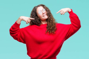 Yüzünde gülümseme ile kendinden emin görünüyorsun, kendini gururlu ve mutlu parmakları ile işaret izole arka plan üzerinde gözlük ve kış kazak giyen güzel esmer kıvırcık saçlı Genç kız.