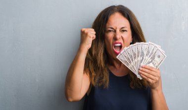 Orta yaş İspanyol kadın dolar tutan gri grunge duvardan ayakta rahatsız ve boşa çıkarmak ile öfke, çılgın da yükseltilmiş el ile bağırmaya kavramı öfke
