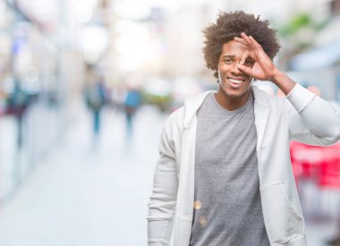 Afro Amerikalı adam gülümsüyor, parmakları ile mutlu yüz üzerinden seyir göz el ile ok jest yapıyor izole arka plan üzerinde Sweatshirt giyiyor.