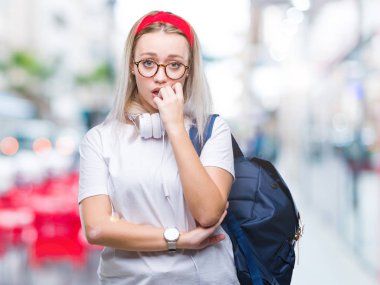 Gözlük ve sırt çantası stresli ve gergin elle çivi ısırma ağzına bakarak izole arka plan üzerinde giyen genç sarışın öğrenci kadın. Anksiyete sorunu.