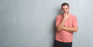 Beyaz delikanlı emin çapraz kollar ve çeneme kaldırdı el ile gülümseme ile kamera seyir gri grunge duvarın üzerinden. Pozitif düşünce.