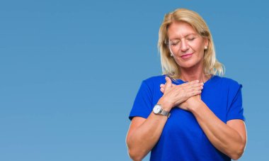 Orta yaş sarışın kadın ile gülümseyen izole arka plan yüzünden kapalı gözler ve yüzünde minnettar jest ile göğüs üzerinde eller. Sağlık kavramı.