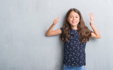 Gösterilen ve parmakları ile işaret grunge gri duvarın üzerinden genç İspanyol çocuğun kendinden emin ve mutlu gülümseyerek süre 6 numara.