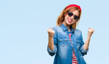 Gülümseyen ve başarı için çığlık genç güzel kadın izole arka plan çok mutlu ve heyecanlı kaldırdı, silah ile kazanan jest yapıyor güneş gözlüğü takıyor. Kutlama kavramı.