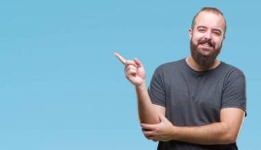 Kameraya bakarak yan el ve parmak ile işaret eden genç beyaz hipster adam yüzünde kocaman bir gülümseme ile izole arka plan üzerinde.