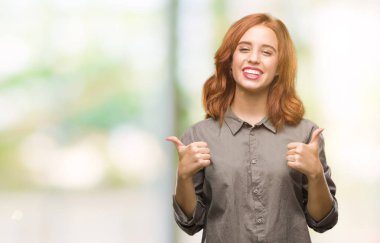 Genç güzel kadın el ile pozitif jest yapıyor izole arka plan başarı işareti yüzünden başparmak gülümseyen ve mutlu. Neşeli bir ifadeyle, kazanan jest kameraya bakıyor.