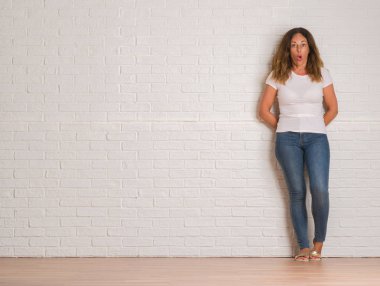 Beyaz tuğla duvar bir sürpriz yüz, korkuyor ve heyecanlı korku ifadesi ile şok korkmuş üzerinde duran orta yaş İspanyol kadın