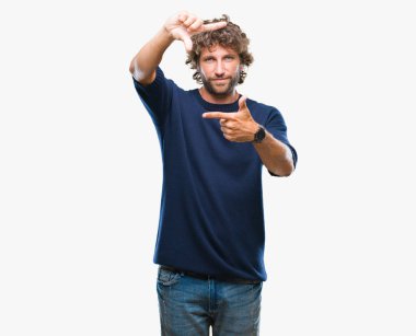 Yakışıklı İspanyol modeli adam elleriyle yapım çerçeve ve parmakları ile mutlu yüz gülümseyen izole arka plan üzerinde kış kazak giyiyor. Yaratıcılık ve Fotoğrafçılık kavramı.
