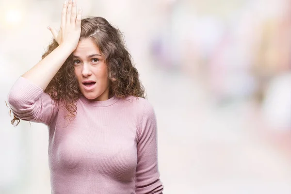 Beautiful brunette curly hair young girl wearing pink sweater over isolated background surprised with hand on head for mistake, remember error. Forgot, bad memory concept.