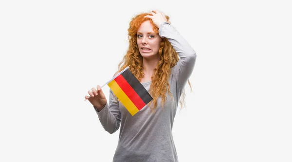 驚きの恥とショックの頭の上の手を強調したドイツの若い赤毛の女性保持フラグ顔 怒っているとイライラします 恐怖と動揺の間違い — ストック写真