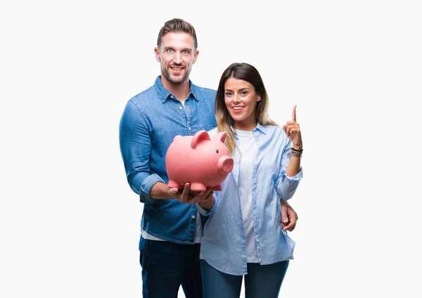 愛持株貯金箱で若いカップル分離背景アイデアに驚いて上銀行や幸せそうな顔 ナンバーワンと人差し指の質問 — ストック写真
