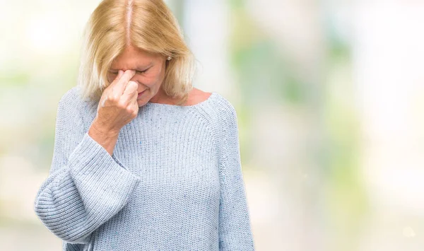 Middle age blonde woman wearing winter sweater over isolated background tired rubbing nose and eyes feeling fatigue and headache. Stress and frustration concept.