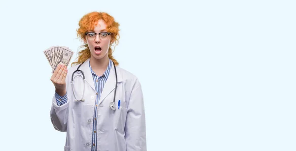 赤毛の若い医師女性驚き顔 恐怖表現と興奮とショックで怖いドルを保有 — ストック写真