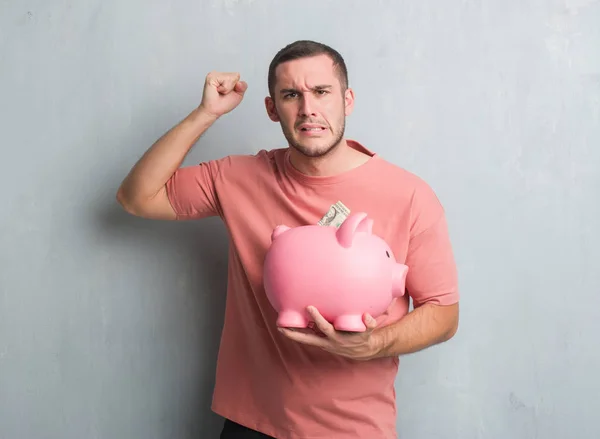 Young Caucasian Man Grey Grunge Wall Holding Piggy Bank Annoyed — Stock Photo, Image