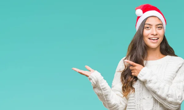 驚くし 手とを提示 指で指している間カメラに笑顔孤立の背景にクリスマスの帽子をかぶって若いアラブ女性 — ストック写真