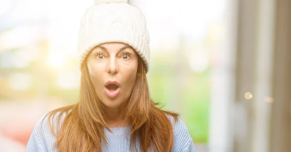 Middle age woman wearing wool winter cap scared in shock, expressing panic and fear