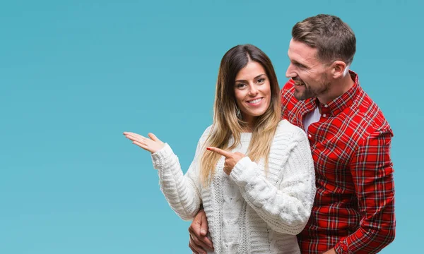年轻夫妇在爱穿冬季毛衣在孤立的背景惊讶和微笑的相机 而提出与手和手指指向 — 图库照片