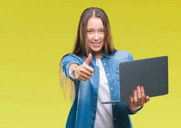 年轻的高加索妇女使用笔记本电脑在孤立的背景高兴与大微笑做确定的迹象 用手指竖起大拇指 优秀的标志 — 图库照片